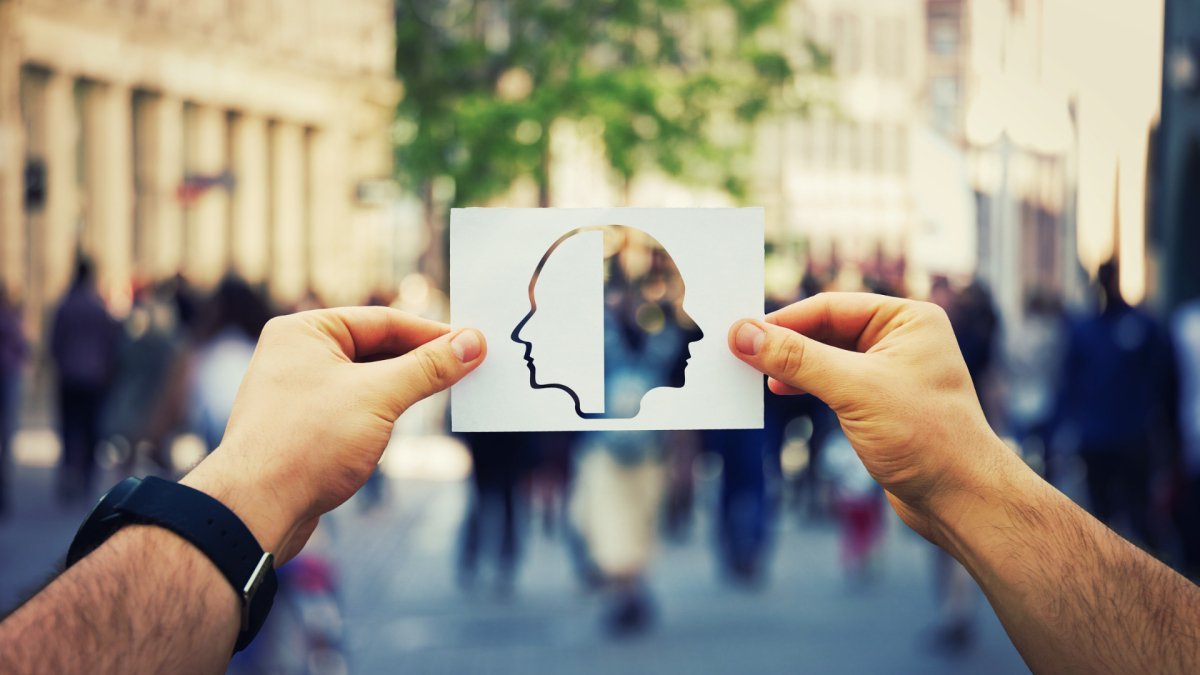 man holding a paper with the outline of face on the left and its mirror cut out on the right, city background