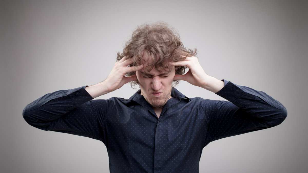 young man holding his head with both of his hands, grey background