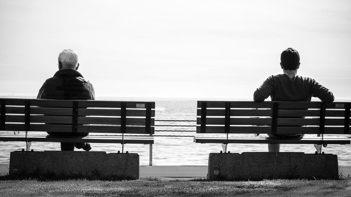 two men sitting on separate benches, ocean view, black and white picture