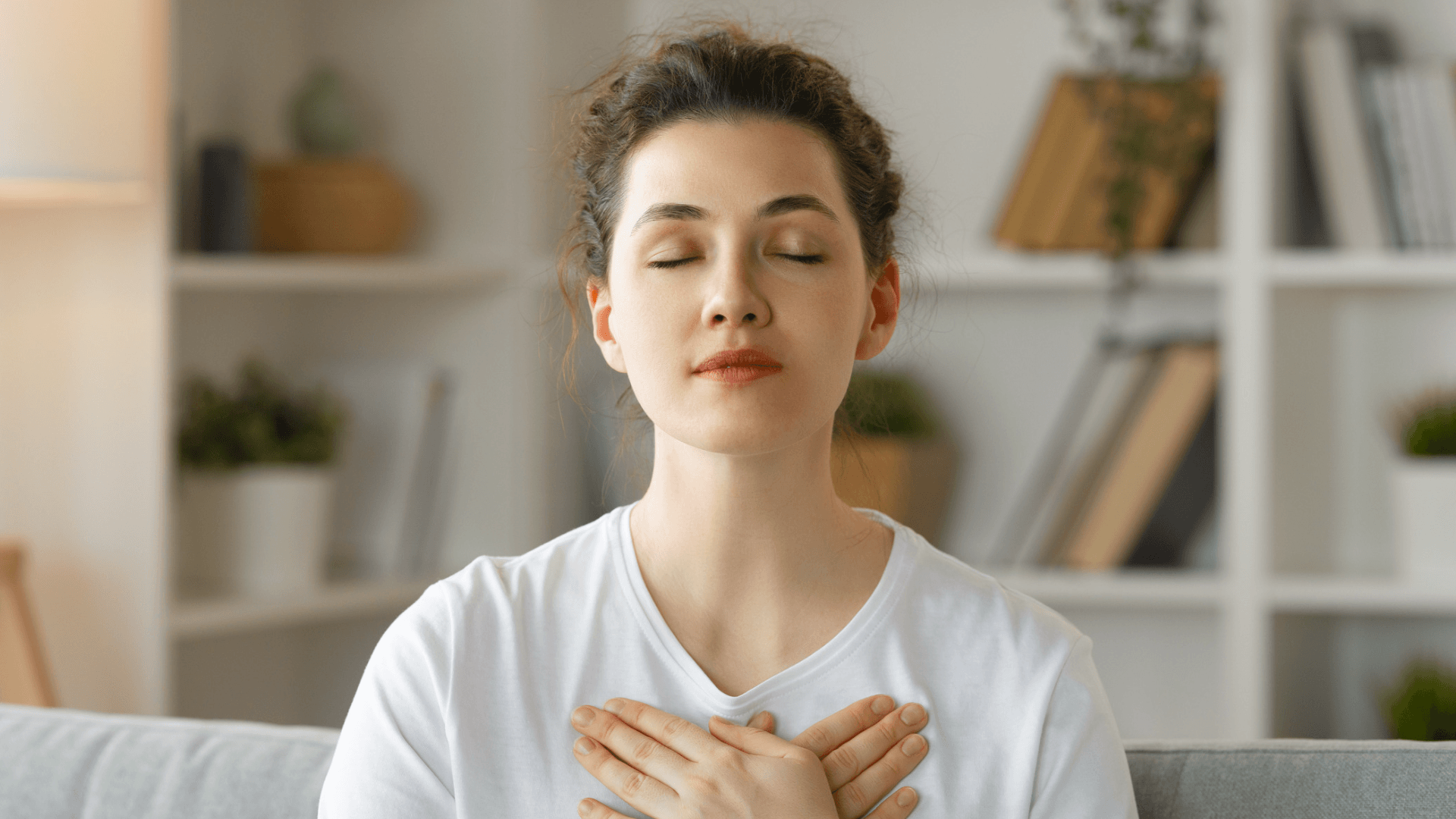 woman with eyes closes, both hands crossed on heart, white t-shit, library background