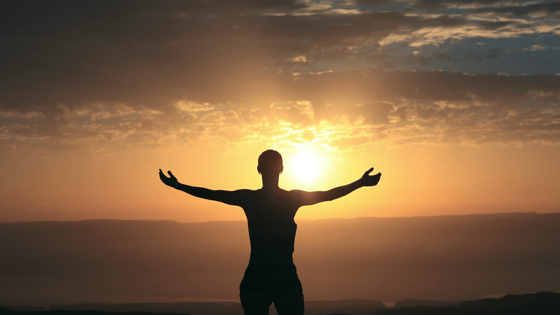 individual with both arms wide open looking at sunset