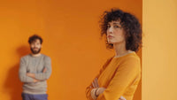 A bold narcissist wife standing near the wall with folded hands, husband blurred in the background
