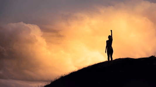 confident woman left arm straight up on a mountain with a cloudy sunset background