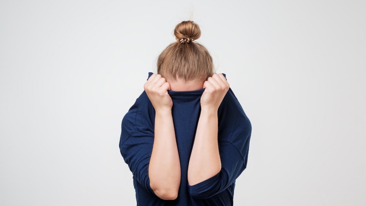 woman pulling her pull-over up and hiding of fear her head