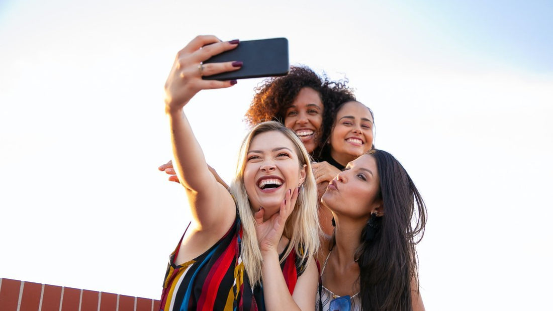 Cheerful girlfriends taking selfie on smartphone on sunny day