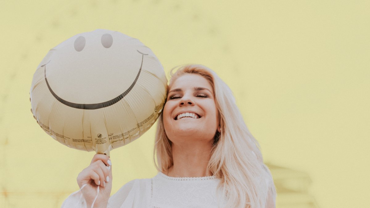 woman smiling holding a happy smiley balloon