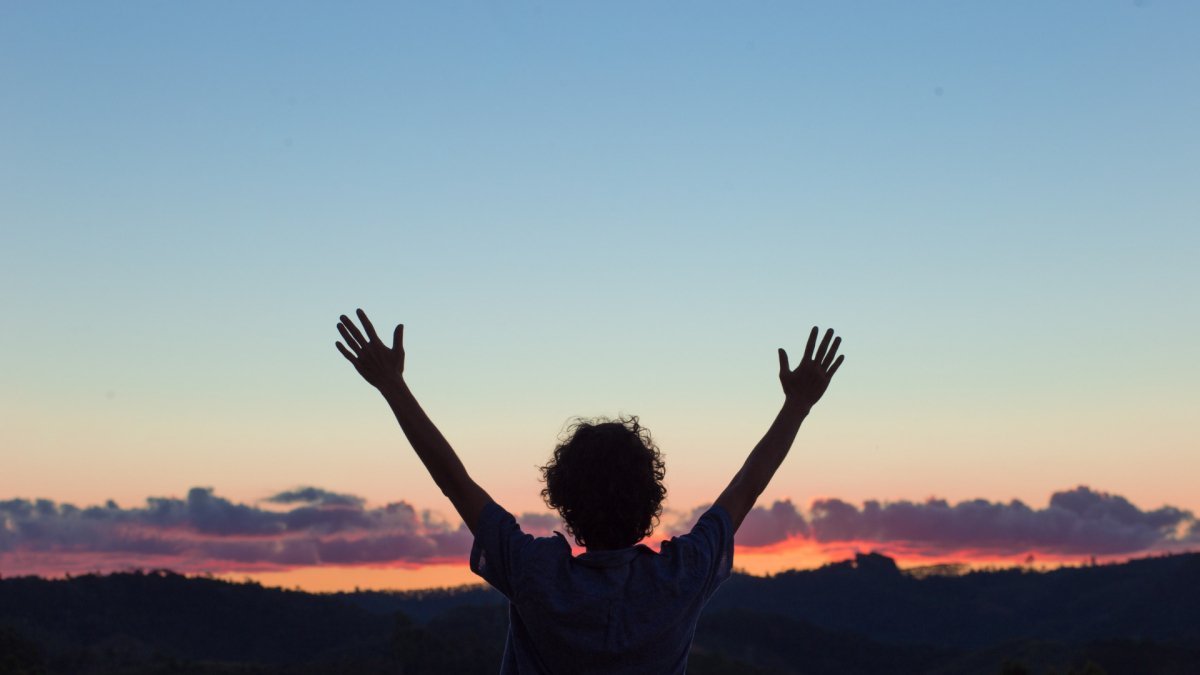 man raising his arms up, sunset view