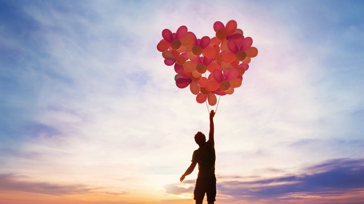 man holding red balloons in the form of heart with sunset background