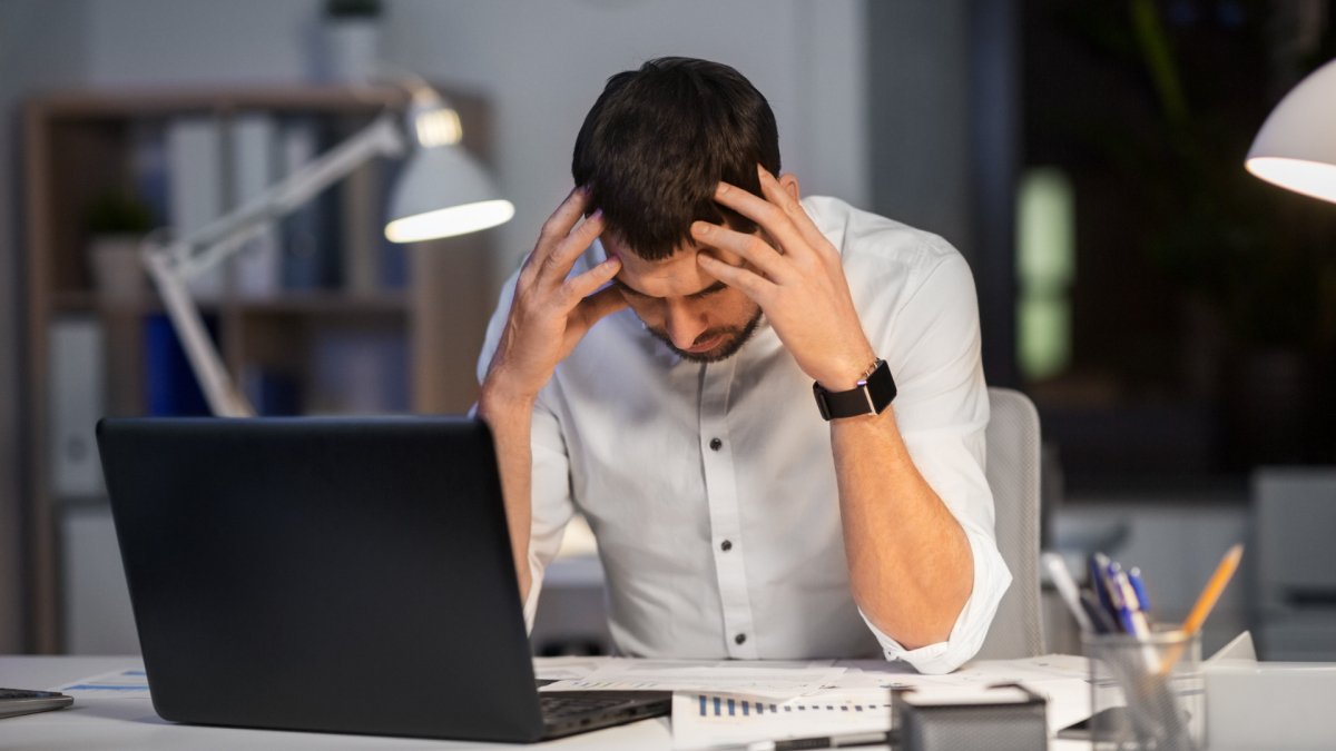 man at desk holding head, signs of work Frustration and stress