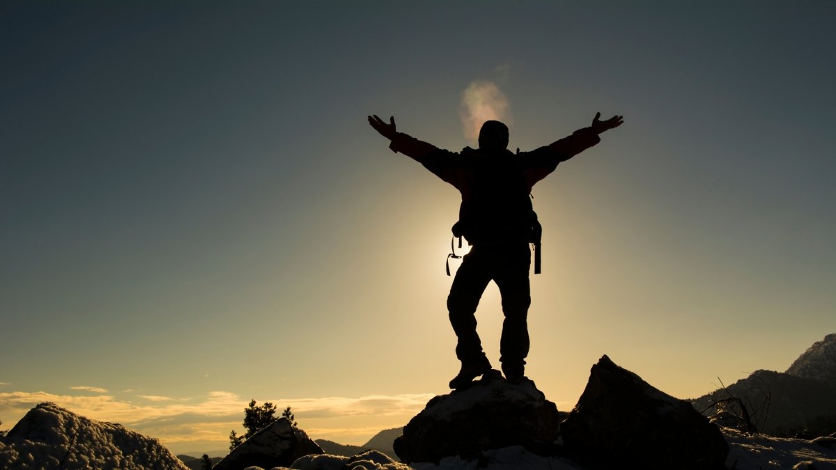 shadow of man on top of mountain with sun behing celebrating his courage
