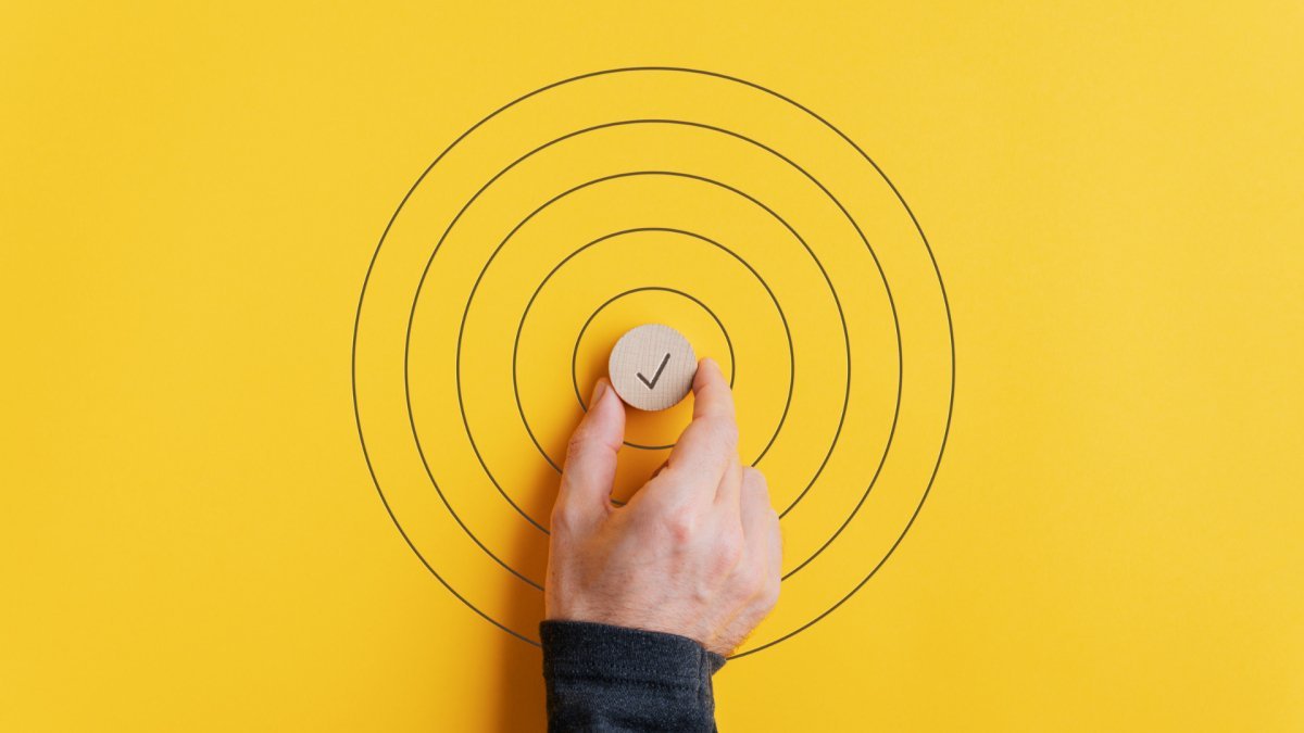 hand putting a wooden check mark in the center of a target drawn on a yellow background