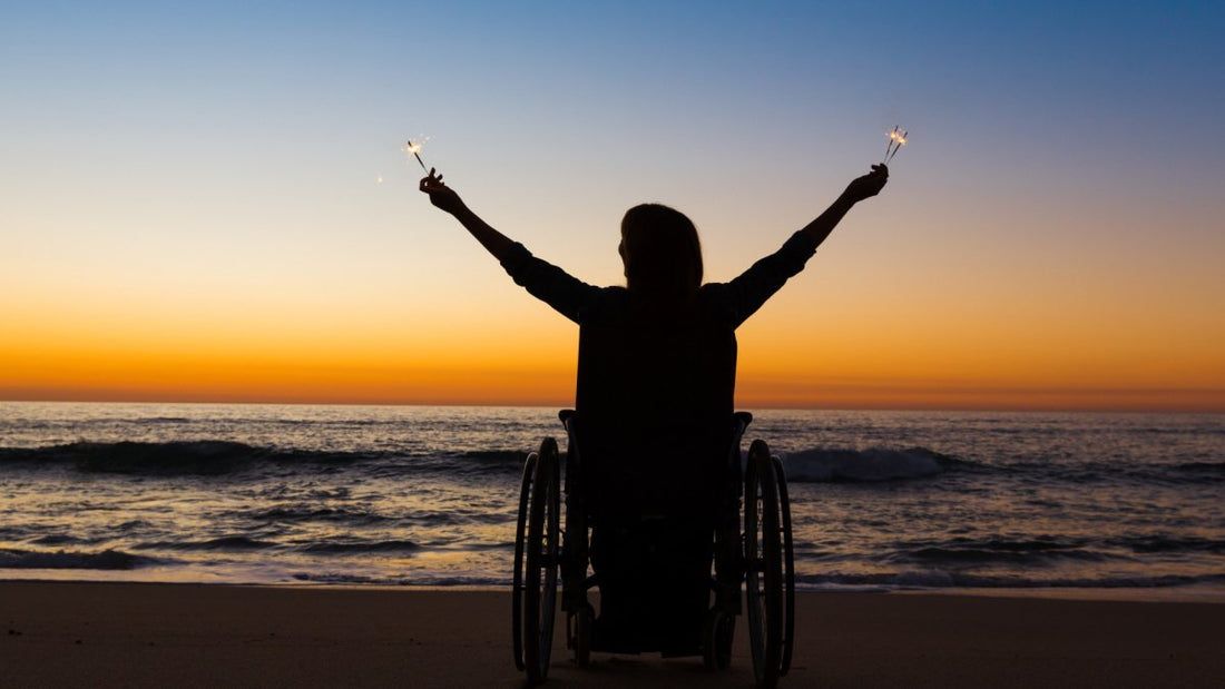 person in a wheel chair celebrating on the beach during sunset