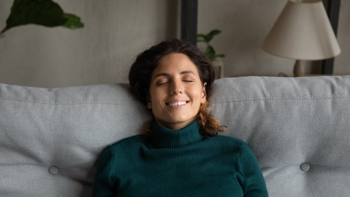woman with a big smile sitting on a grey couch, head resting, in tune with her emotions 