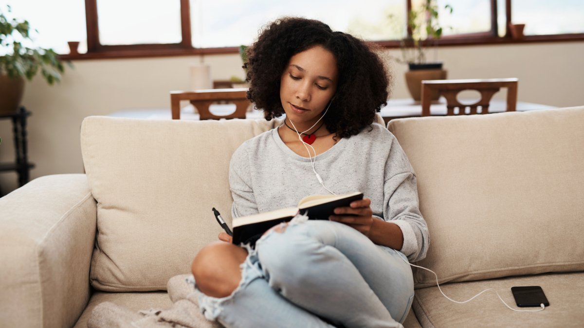 woman sitting on a couch listening to music writing down her intentions aspirations on a journal