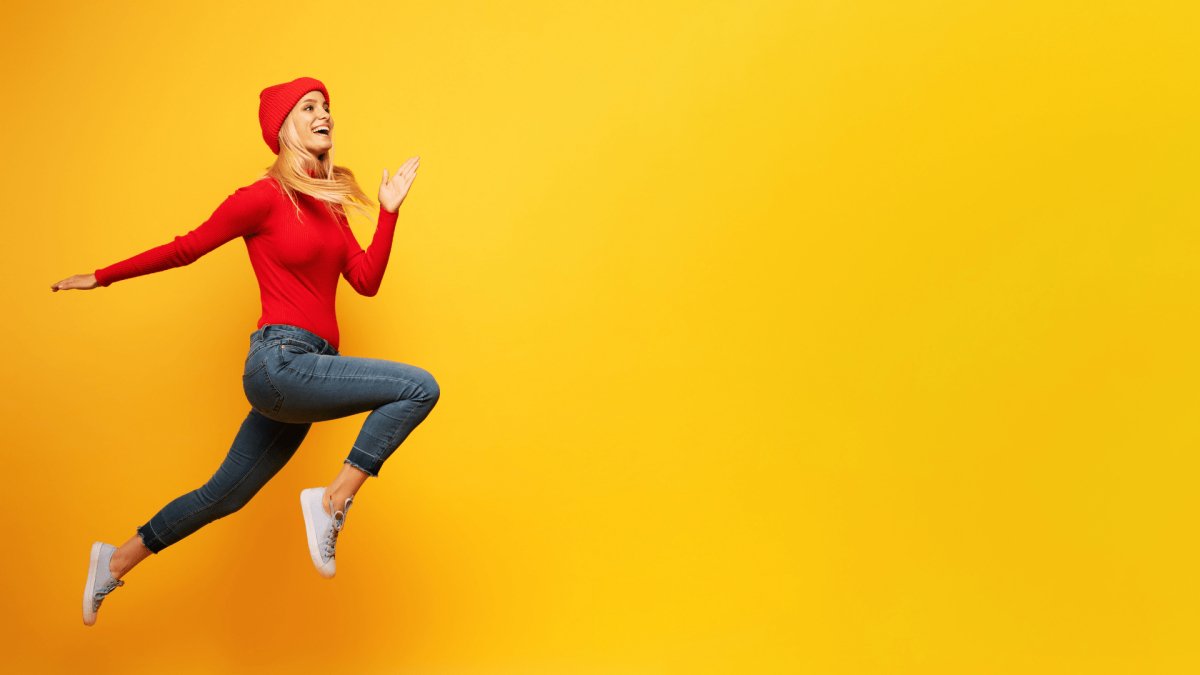 woman dressed up in red jumping happy face positive energy with an orange background