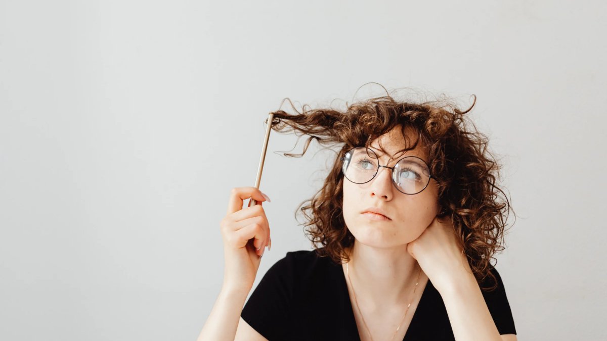 Woman thinking with glasses and a pencil in her hair 