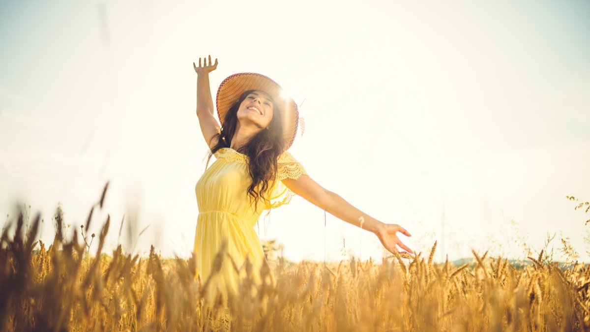woman wearing a hat in a wheat field feeling happy and living with authenticity for herself