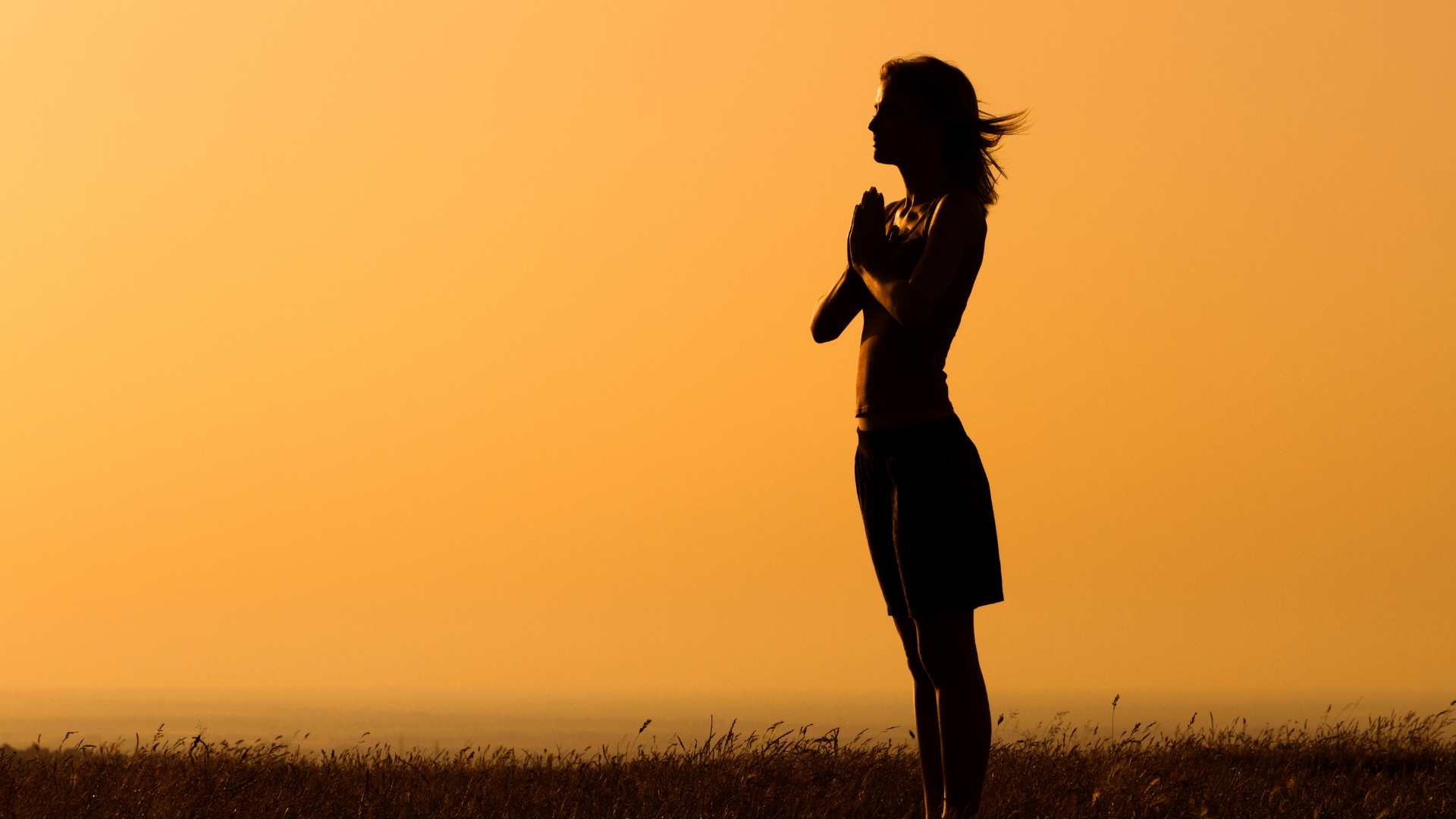 woman standing, hands joined with a quiet mind, sunset background