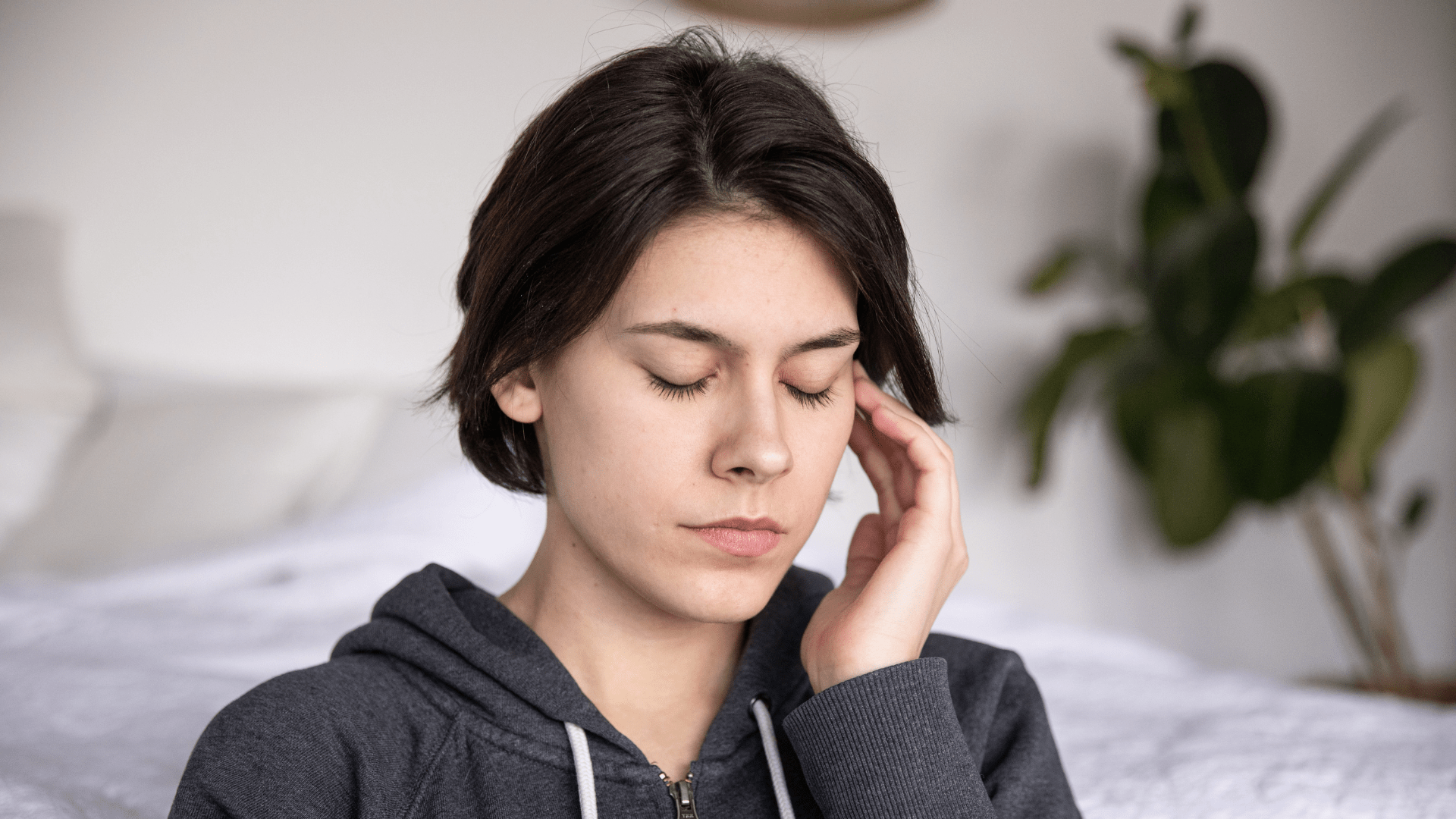 woman eyes closed overthinking with her left fingers on the side on of her heard