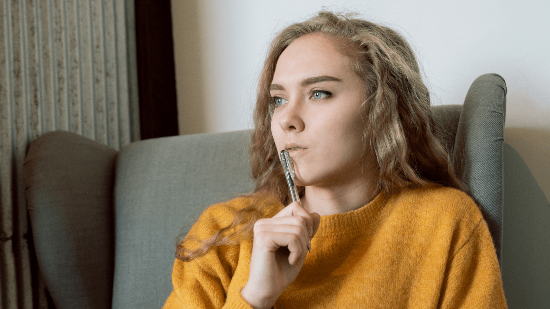woman with orange sweater thinking holding a pen to her mouth