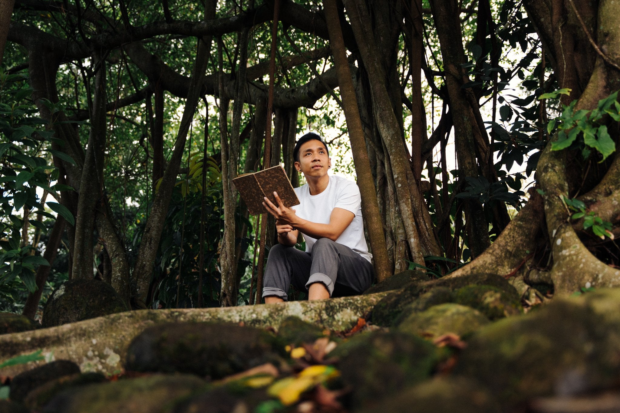 Bayu coach at Life Architekture, wearing white t-shirt, face sideways, holding book, in jungle background