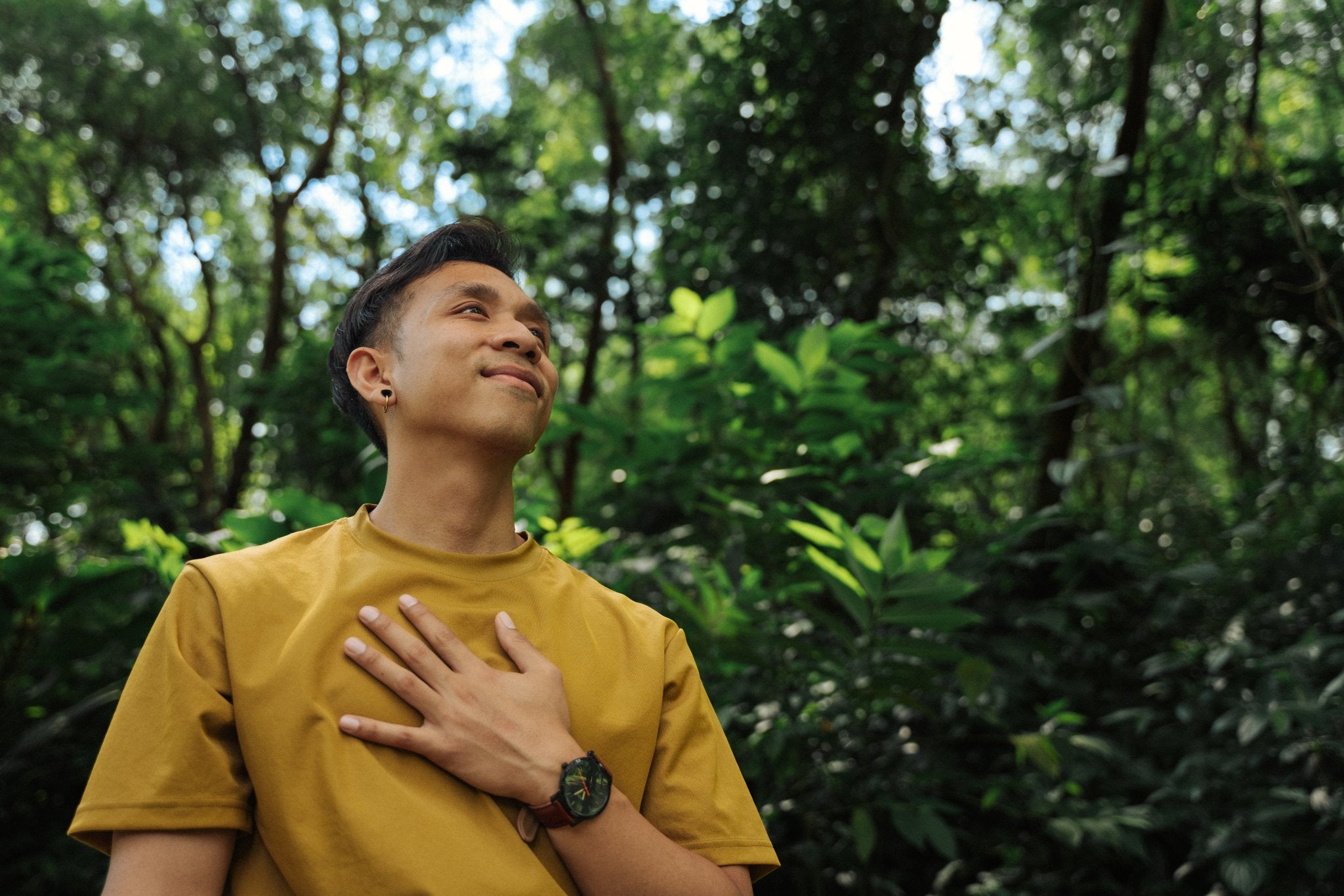 Bayu coach at Life Architekture, wearing yellow t-shirt, face looking up, hand on heart, in jungle background