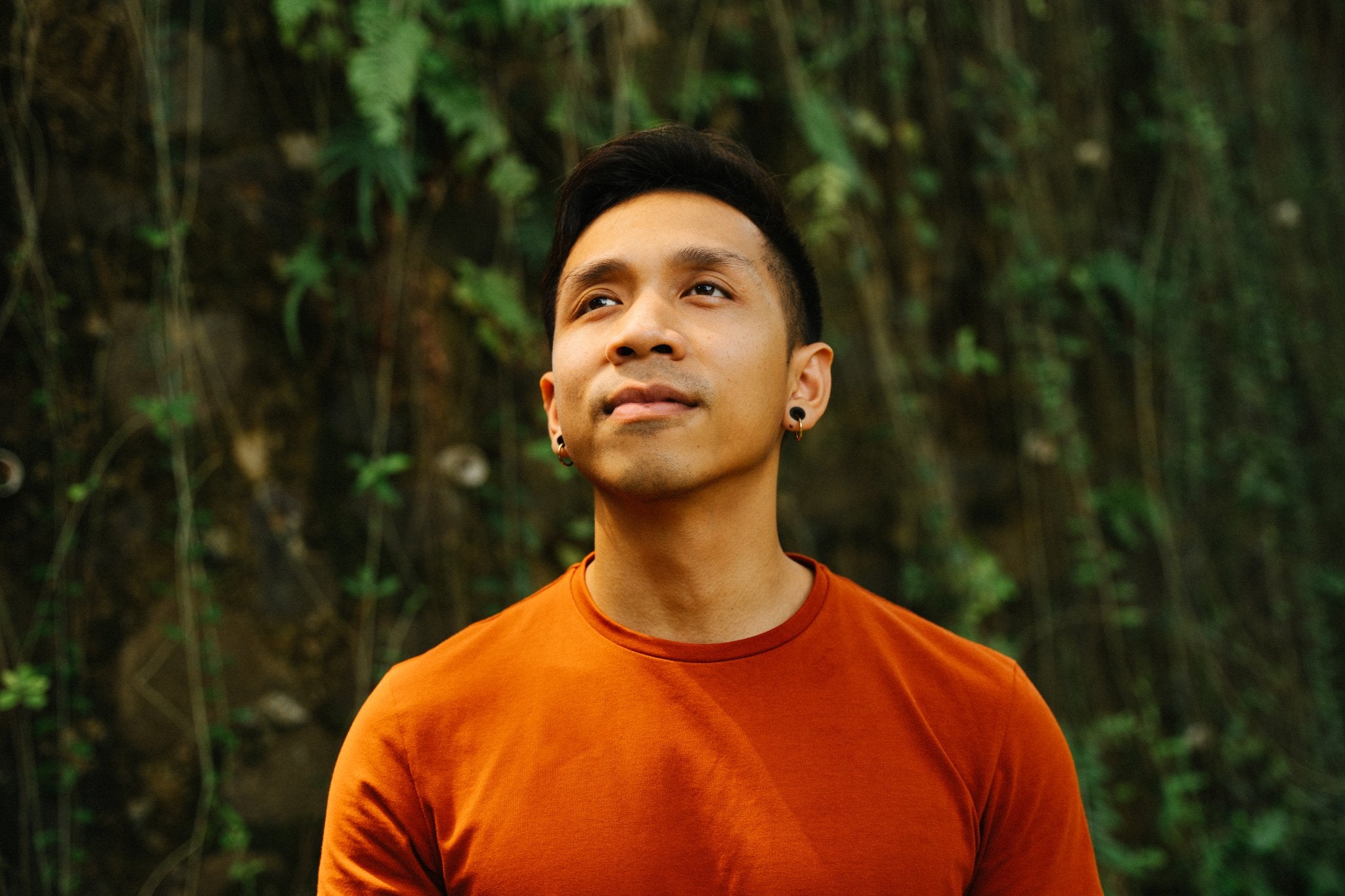 Bayu coach at Life Architekture, wearing orange t-shirt, face looking up, in jungle stone wall background