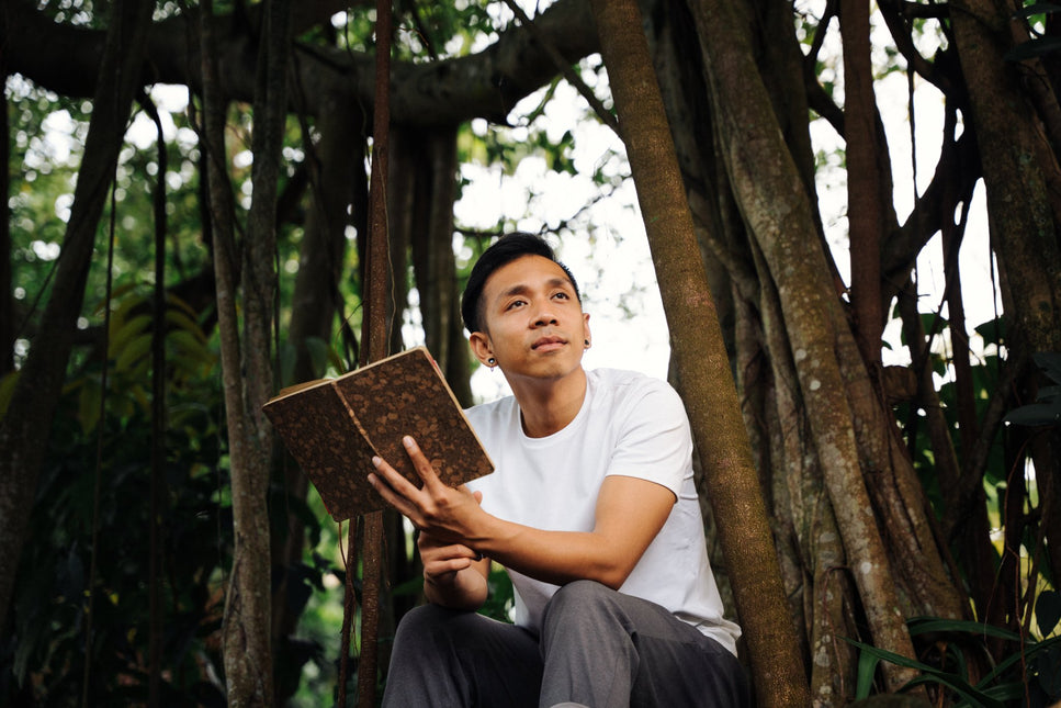 Bayu coach at Life Architekture, wearing white t-shirt, holding a book, looking away, in jungle background
