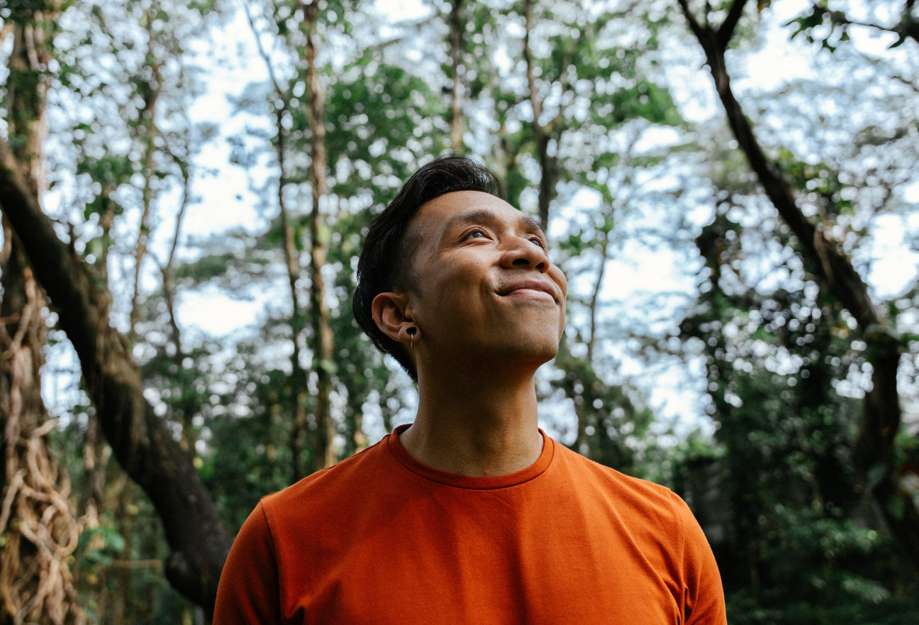 Bayu coach at Life Architekture, wearing orange t-shirt, face looking up, smiling, in jungle background